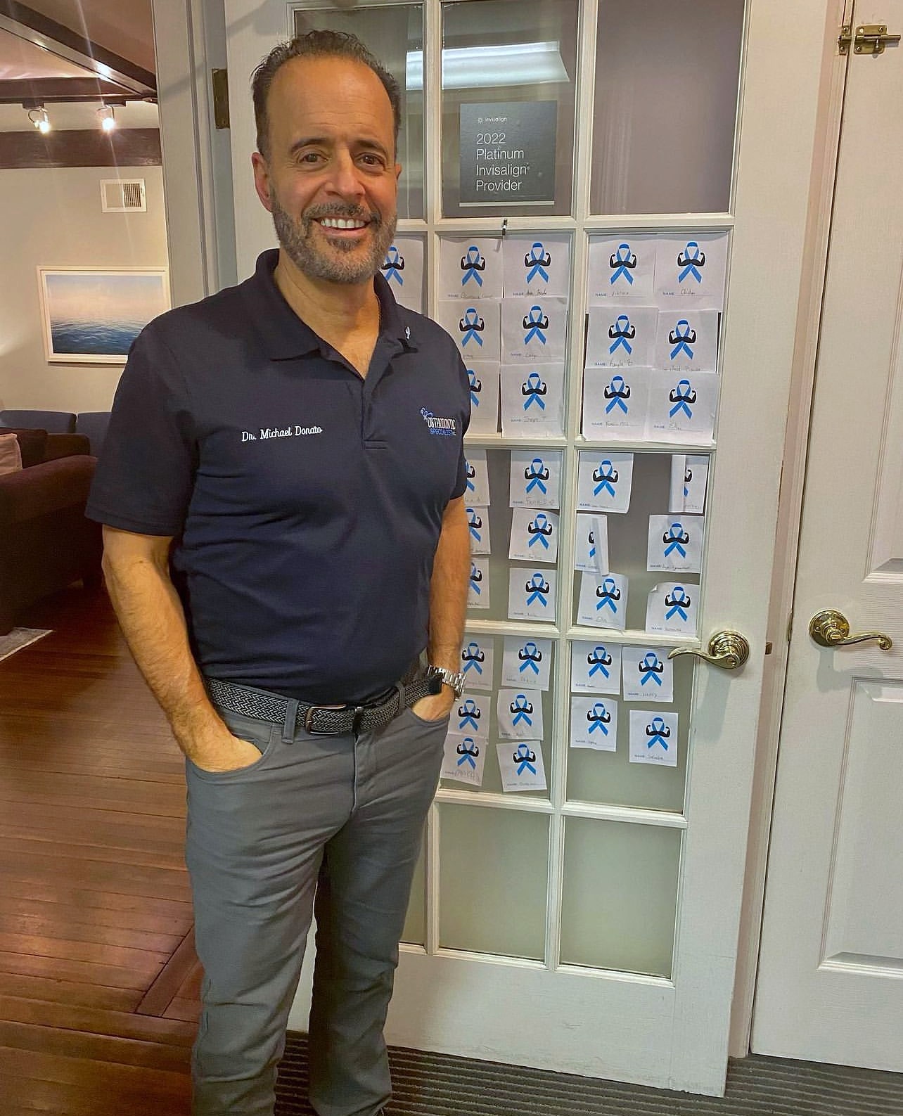 Orthodontist in logo polo standing by door covered in ribbon cards