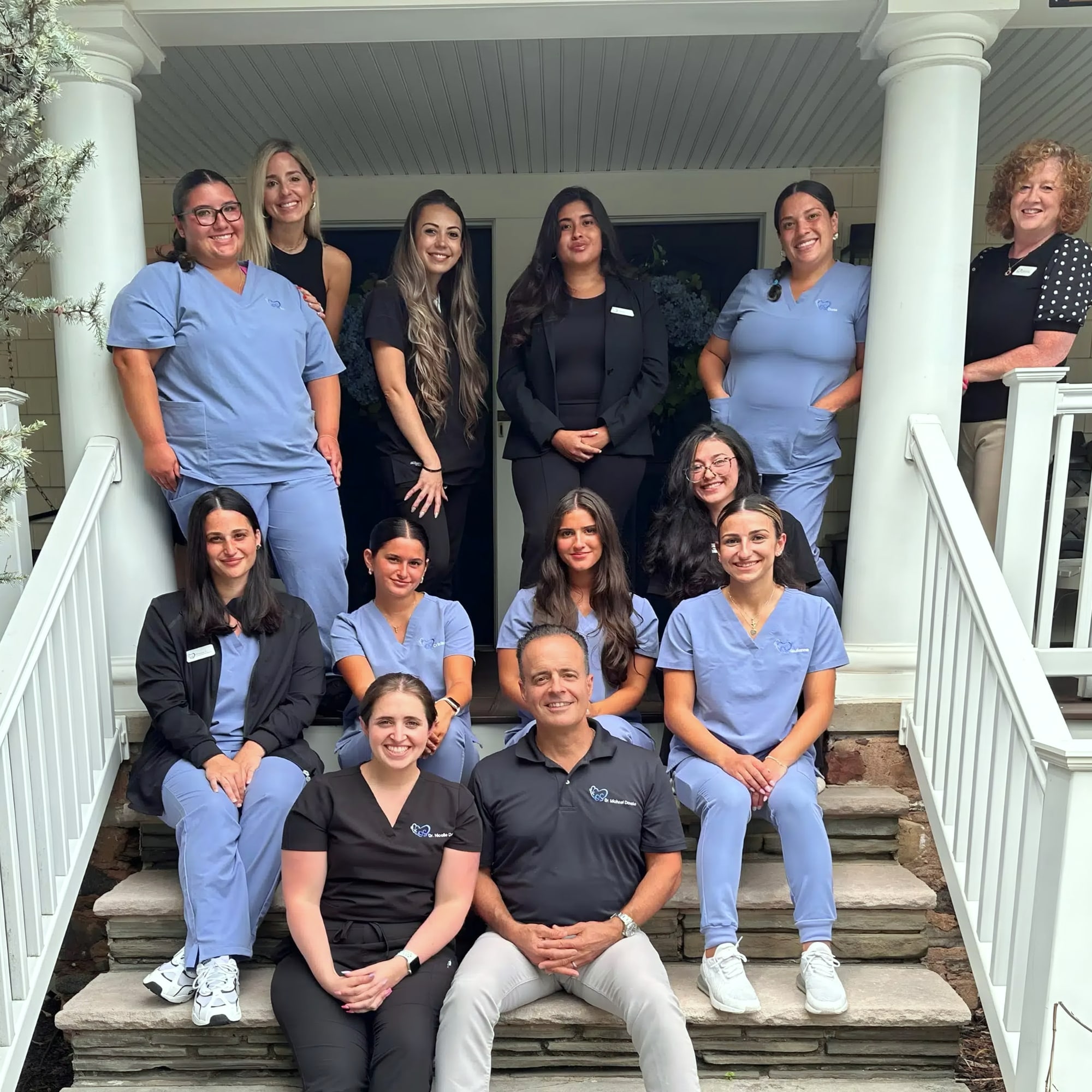 Group of twelve staff in scrubs posed on porch steps